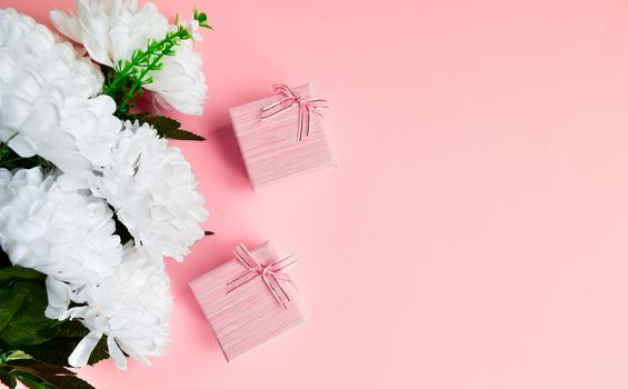Two pink gift box with golden ribbon bow. Bouquet of white flowers. Gifting elegant concept on pink background, with copy space.