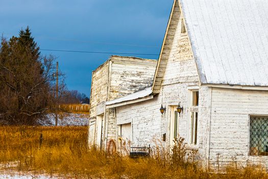 An old rural house is run down and has white peeling paint on aged wooden walls.