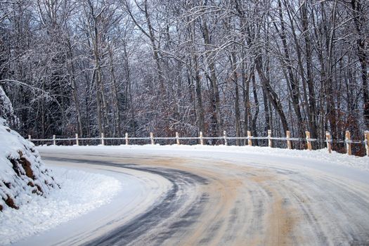 A rural road running up the side of a hill is seen in the winter, covered in snow and the tracks of previous vehicles. The road turns as it follows the hillside curves.