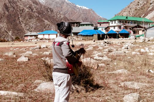 A solo traveler hobbyist musician playing guitar alone in the silence of Himalayan mountain valley and sound of guitar strings. Summer music Inspiring environment in outdoors. Sangla India South Asia.
