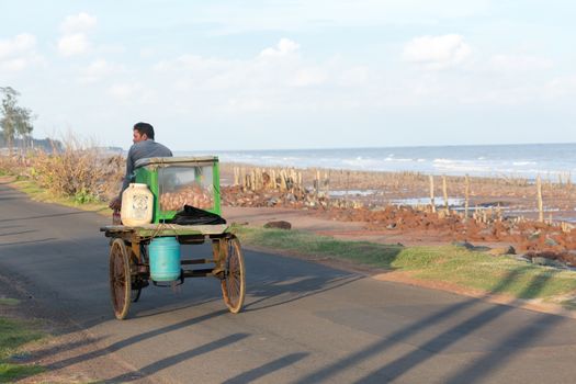 A rural local village mobile street food seller selling phuchka, gol gappa, chaat and pani puri on traditional cycle rickshaw van vehicle in coastal area beach road in summer sunset. India, May 2019
