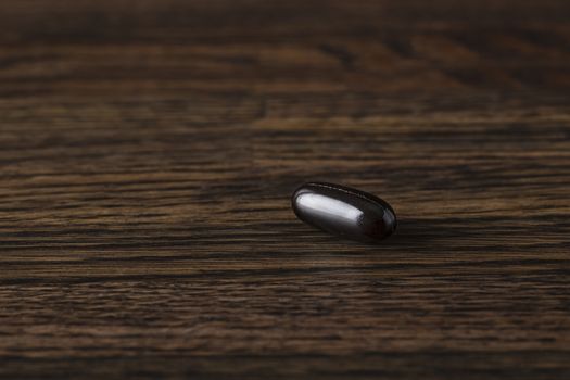 close-up of a large black omega 3 pill against a dark wood background