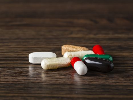close-up of a selection pill, tablet & capsule against a dark wood background