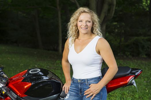 Twenty something woman, wearing a white tank top, outdoor in a park, beside a motocycle