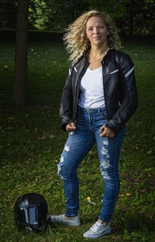 twenty something blond woman wearing a motocycle leather jacket with a helmet by her feets