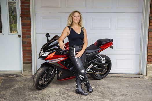 twenty something blond woman wearing leather pant and a black tank top, doing a duck face, while leaning on a sport motocycle