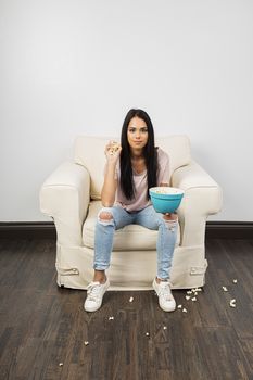 Young woman holding a handfull of popcorn, sitting on a couch