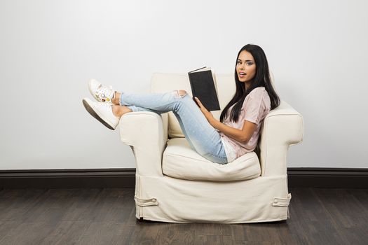 twenty something woman, with her legs up on a couch, reading a hard cover book