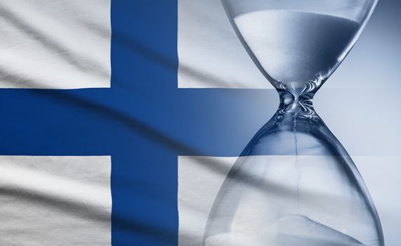 Flag of Finland with superimposed hourglass with running sand conceptual of deadlines, countdown, passing time, urgency, crisis and time management