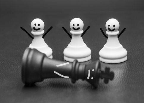 Three chess piece pawns with smiles and raised arms rejoicing at a fallen king in front of them in a conceptual image