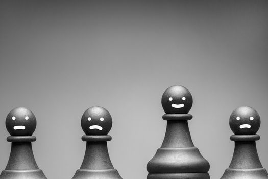 Greyscale image of chess pieces with faces showing happy, neutral and cross expressions on pawns with copy space above