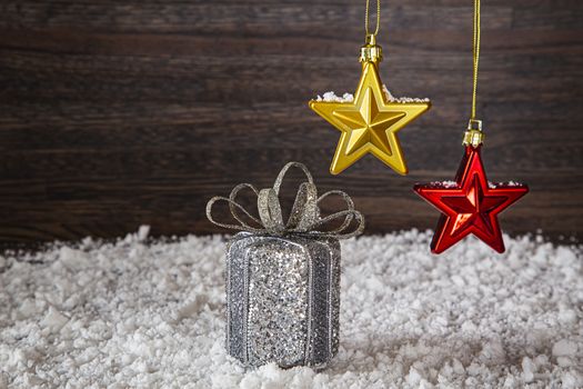 silver wrap present with bow, in the snow, with two star decoration