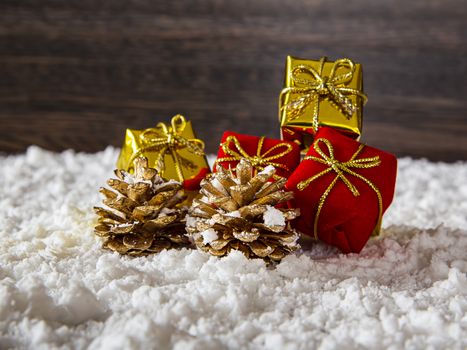 two golden pine cone with red and gold present in the snow against a wood background