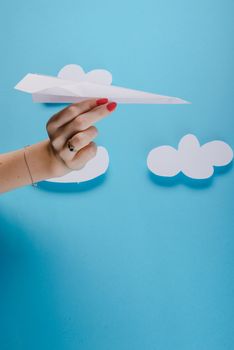 Paper plane in female hand on a blue background with clouds