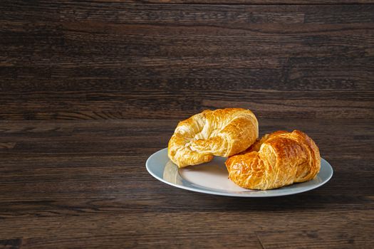 two croissant on a blue rim plate on a dark wood background