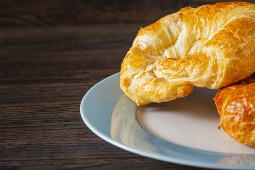 close up shot of a croissant on a blue rimmed plate against a dark brown wood background
