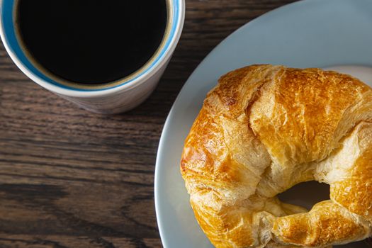 top view of a cup of coffee and a croissant on a plate