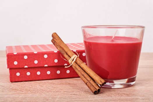 Close up shot of a gift box, aromatic red candle and cinnamon sticks on a wooded table.