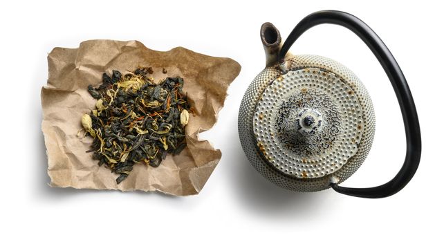 Green tea with natural aromatic additives and a teapot. Top view on white background.