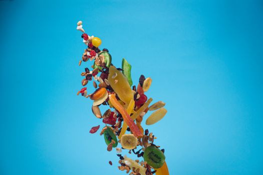 Dried and candied fruits and nuts flying on blue background. Stock photo of healty and nutrient food. Conceptual photo of vegan and vegetarian healty food.