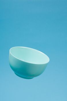A blue ceramic mattle deep bowl for breakfast flying on blue background. Ideal photo for levitation of food and fruits or nuts.