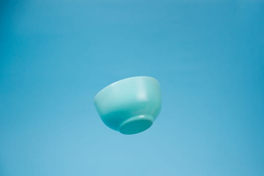 A blue ceramic mattle deep bowl for breakfast flying on blue background. Ideal photo for levitation of food and fruits or nuts.