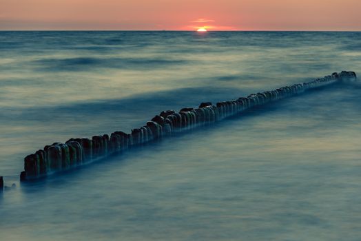 A photograph of wooden breakwater and seagulls at sunset on the Baltic Sea