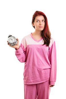 Portrait of a beautiful young girl in pink pajamas holding an alarm clock looking annoyed that she needs to get up, isolated on white background.