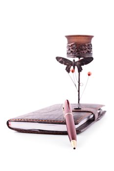 Close up of a planner notebook with a pen and an old fashioned candle holder, isolated on white background.