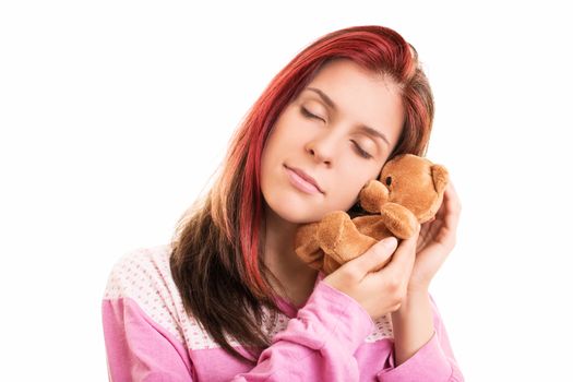 Close up of a young beautiful girl in pink pajamas hugging a plush brown teddy bear, isolated on a white background.