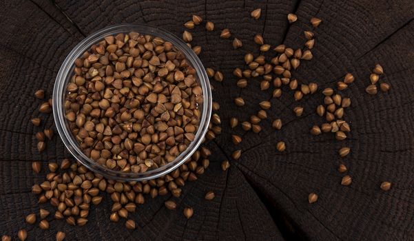 Bowl of buckwheat grains on black wooden background, top view