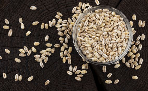 Bowl of pearl barley on black wooden background, top view