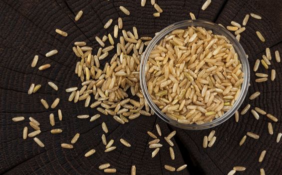 Bowl of brown rice groats on black wooden background, top view