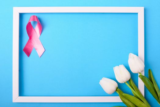 Breast cancer month concept, flat lay top view, pink ribbon and Tulip Flower with photo frame on blue background with copy space for your text