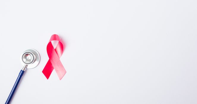 Breast cancer month concept, flat lay top view, pink ribbon and stethoscope on white background with copy space for your text