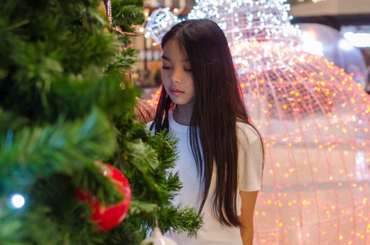Asian teenage girl wearing a white shirt stands above the Christmas tree.