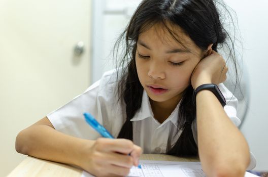 Beautiful young Asian girl wearing a school uniform was intended homework at the table.