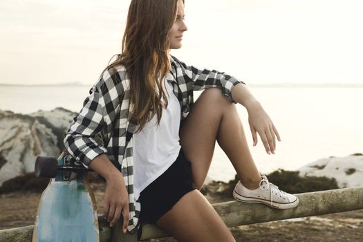 Beautiful and fashion young woman posing at the sunset with a skateboard