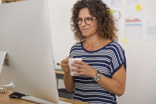 Portrait of a middle aged woman at the office drinking coffee