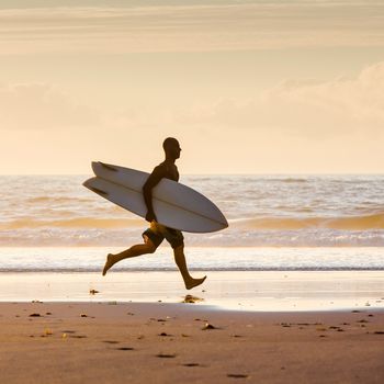 Surfer on the beach running with is surfbard ready to surf