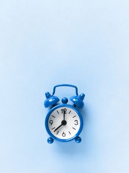 Small alarm clock on pastel background in Classic Blue colour, close-up, top view. Minimal retro style. Time management, Color of the year 2020 concept. Copy space for text. Vertical orientation.