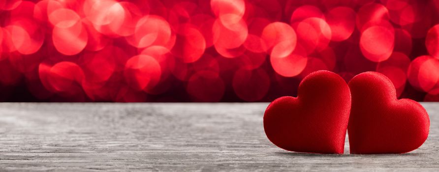 Valentine's day two red silk hearts on wooden background and bokeh lights, love concept