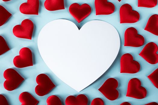Valentine's day many red silk hearts and white heart shaped card on blue background, love concept