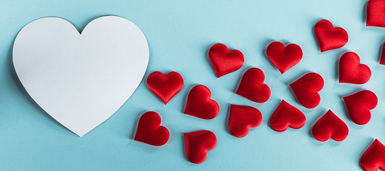 Valentine's day many red silk hearts and white heart shape card on blue paper background , border frame on red with copy space, love concept