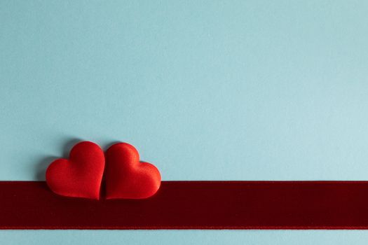 Valentine's day two red silk hearts and red satin ribbon on blue paper background, love concept