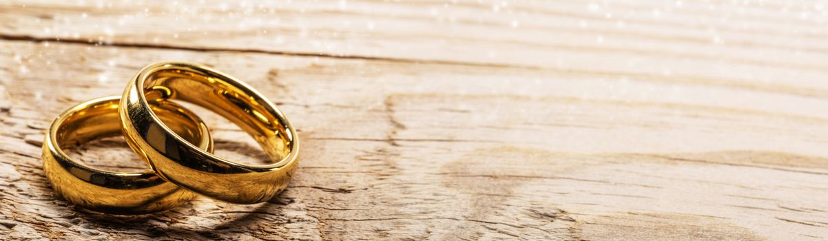 Two golden wedding rings on wooden background with copy space for text