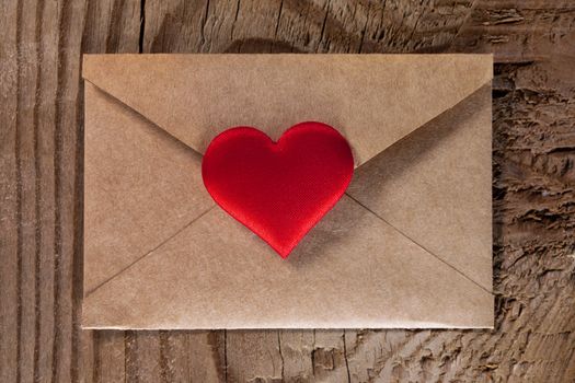 Valentine day love letter, envelope of craft paper with red heart on wooden background