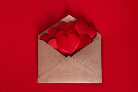 Valentine day love letter, envelope of craft paper with red hearts heap spread on white background.