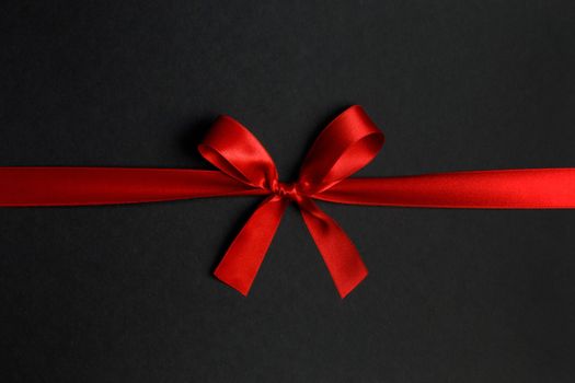 Red satin ribbon bow on black paper background