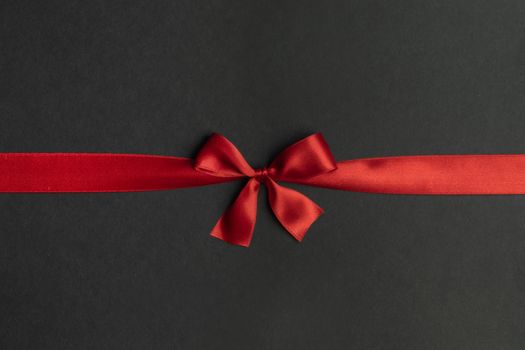 Red satin ribbon bow on black paper background